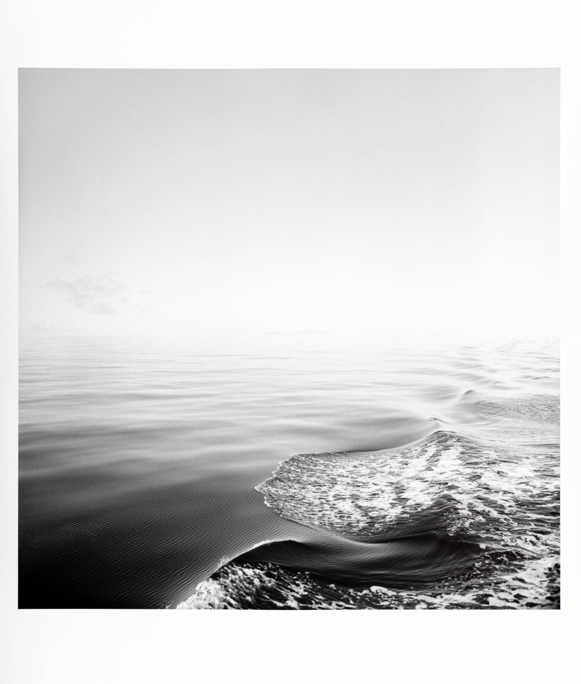 A black and white photograph of waves. The water is smoother on the left side of the photo than on the right.